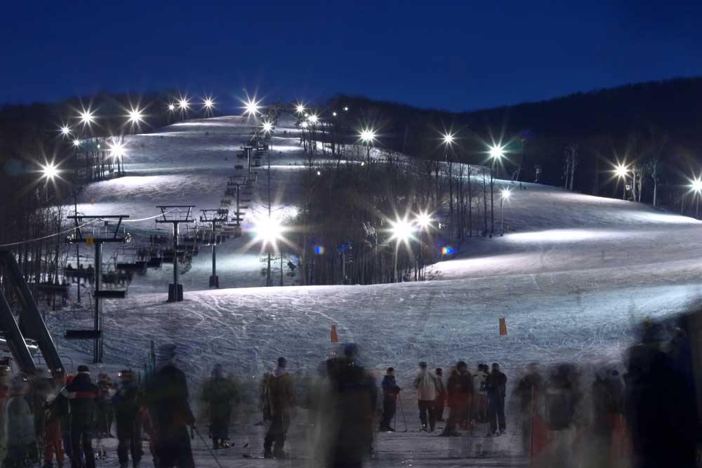 High mast LED lighting illuminates a ski slope at a resort after dark